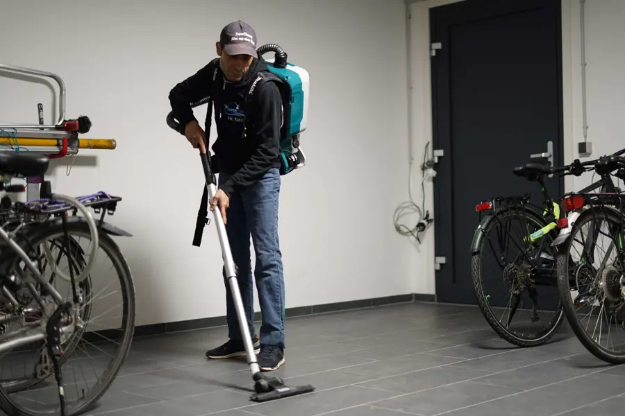 Mitarbeiter von SuperCleanup saugt mit einem Rucksackstaubsauger den Boden eines Eingangsbereichs
