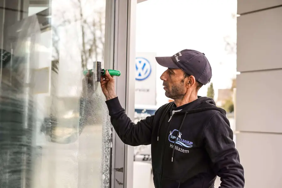 Mitarbeiter von SuperCleanup reinigt mit dem Abzieher eine Glastür am Eingang
