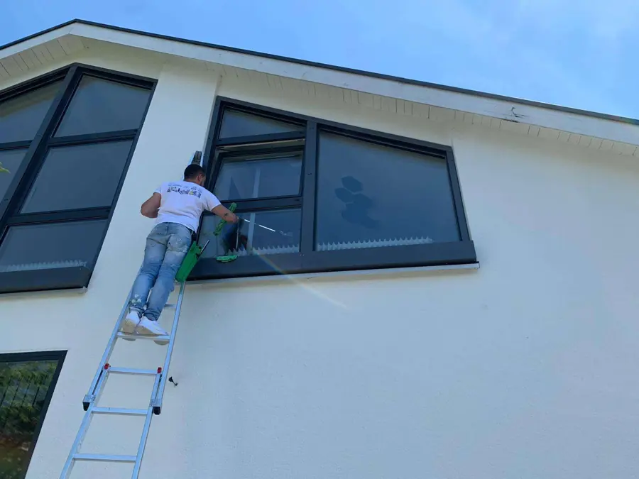 Mitarbeiter von SuperCleanup reinigt auf einer Leiter die Fenster eines Wohnhauses