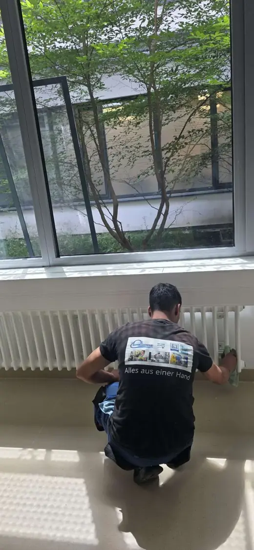 Mitarbeiter von SuperCleanup reinigt knieend den Bereich unter einer Fensterfront
