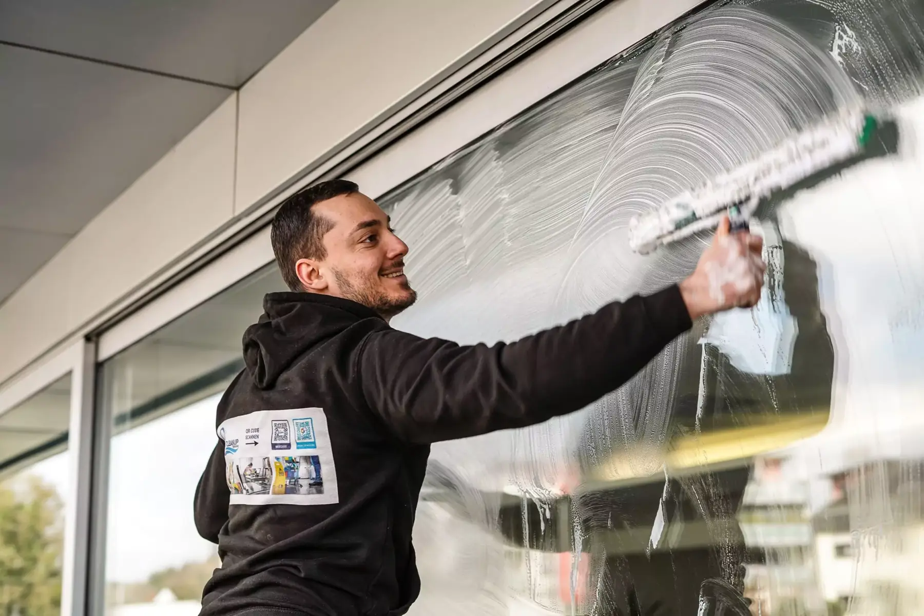 Mitarbeiter von SuperCleanup zieht mit dem Abzieher eine eingeschäumte Schaufensterscheibe ab